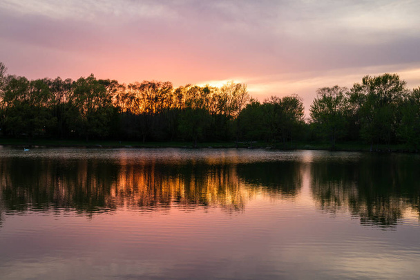 rustige zonsondergang nadenken over een vijver met warme tinten weerkaatst op de wolken en water - Foto, afbeelding