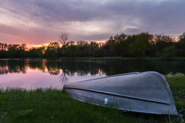 zonsondergang nadenken over een vijver met een kleine peddel boot op de met gras begroeide, groene oever - Foto, afbeelding