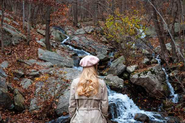 Mulher bonita em roupas quentes de outono está olhando para waterfal na floresta. Conceito de viagem
 - Foto, Imagem