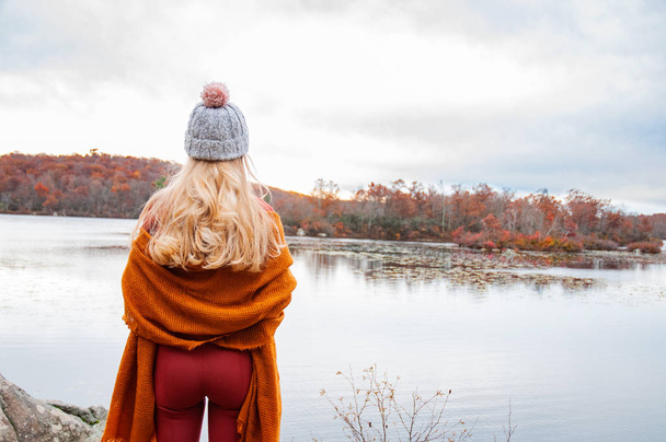 Woman traveler in warm hat and autumn clothes looking at amazing lake and forest, wanderlust travel concept - Valokuva, kuva