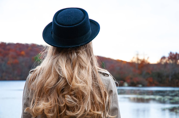 Woman in hat and warm autumn clothes looking at amazing lake and forest, wanderlust travel concept - Фото, изображение