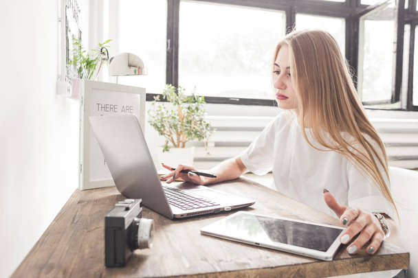 Young business woman working at home behind a laptop and tablet. Creative Scandinavian style workspace - Photo, image