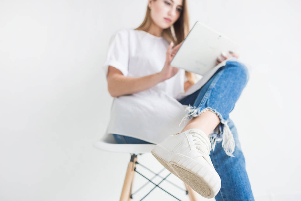 Portrait of a young stylish blonde girl in a white T-shirt and blue jeans using a tablet on a white background - Valokuva, kuva