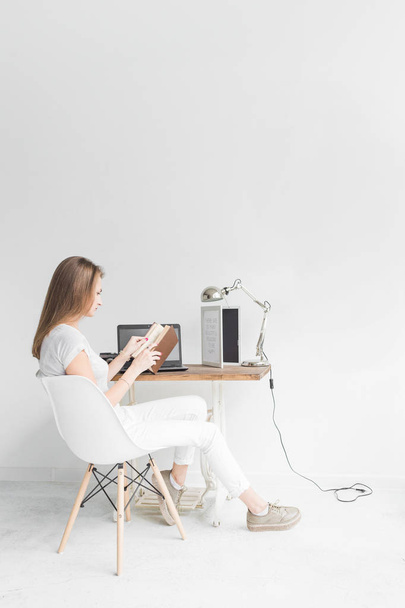 Young business woman working at home and reading a book. Creative Scandinavian style workspace - 写真・画像