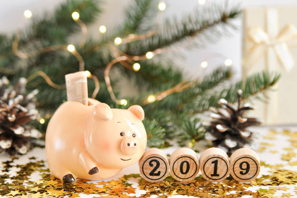 Lustiges Sparschwein mit dem Geldsymbol des neuen Jahres 2019 auf dem Hintergrund von Tannenzweigen, die mit Lichtern und leuchtenden Sternen geschmückt sind. Chinesisches Neujahr. Kopierraum für Text - Foto, Bild
