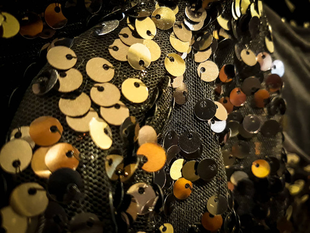 Блестящие серебряные и желтые круглые пластины над темной сеткой. Браслет, ожерелье, украшения
. - Фото, изображение