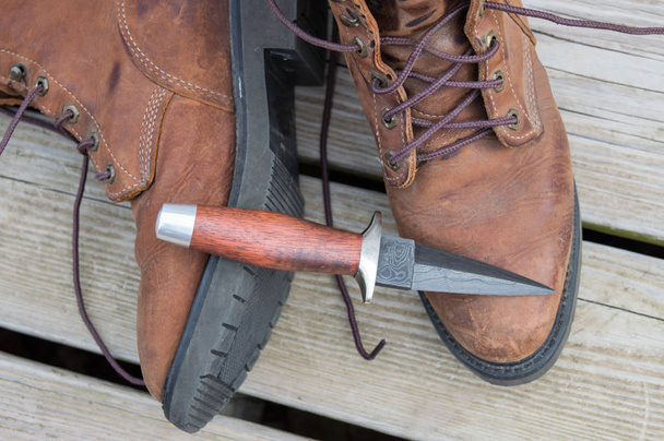 Un cuchillo de arranque que se muestra en botas de trabajo
. - Foto, imagen