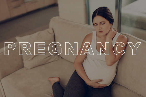 Parturient Girl Clings to Stomach. Pregnant Woman Stiff Neck. Daily Life Expectant Mother. Expectant Mother Get Well. Preggers Sit at Home. Pregnant Female on Light Sofa. Frown Pregnant Woman. - Photo, Image