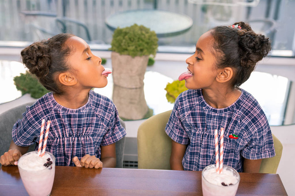 Two curly dark-haired siblings playing tricks spending time in kids cafe - Fotó, kép