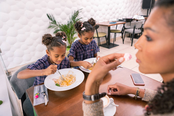 Dark-haired mother feeling thoughtful while her children eating lunch - Photo, Image