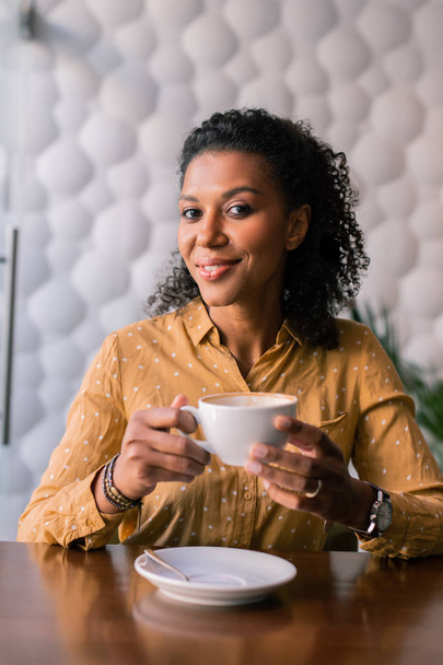 Stylish woman wearing accessories and yellow blouse drinking coffee - Photo, Image
