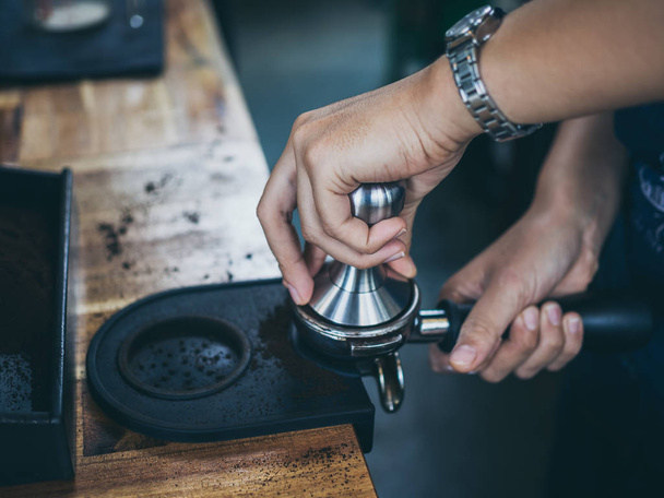 Επαγγελματική barista χέρια πιέζοντας λόγους καφέ με τάμπερ στο ξύλινο τραπέζι στην καφετέρια. - Φωτογραφία, εικόνα