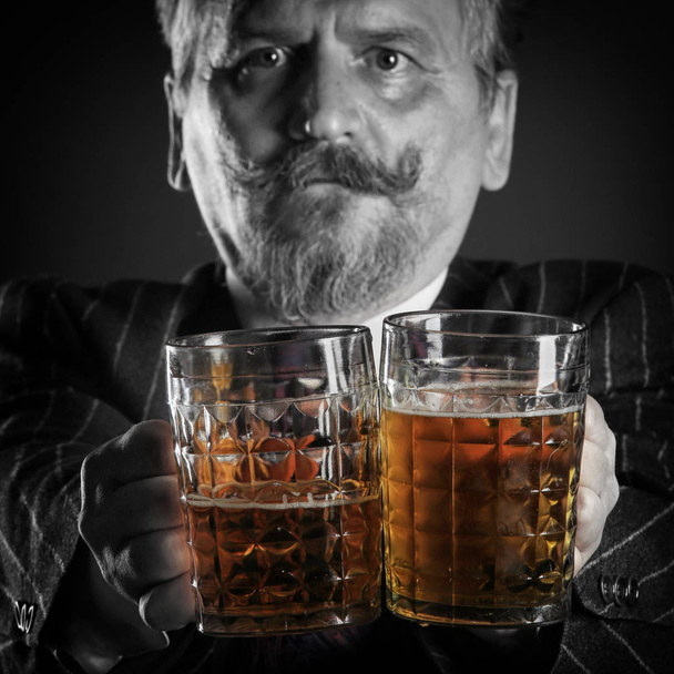 closeup portrait of an adult male with a mustache and beard, wearing glasses and a business suit with beer mug - Fotó, kép