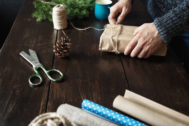 Male hands preparing Christmas present on wooden table. Rustic Christmas background - 写真・画像
