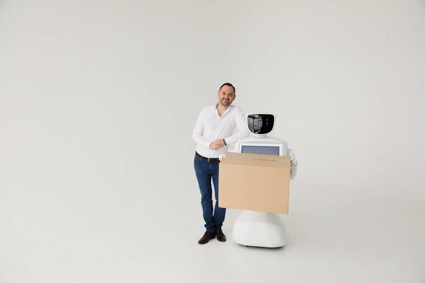 Modern Robotic Technologies. A man communicates with a robot, with cardboard box in hand. - Foto, immagini