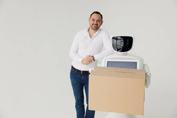 Modern Robotic Technologies. A man communicates with a robot, with cardboard box in hand. - Фото, зображення