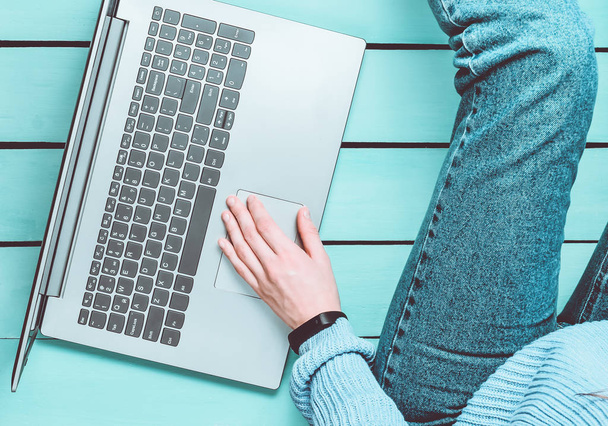 Een moderne meisje zit op een blauwe houten vloer en maakt gebruik van een laptop. Generatie z. Het concept van freelancen. Werkruimte. Bovenaanzicht. - Foto, afbeelding