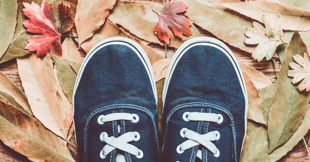 Hipster blauwe sneakers op een houten vloer tegen een achtergrond van gele gevallen bladeren. - Foto, afbeelding
