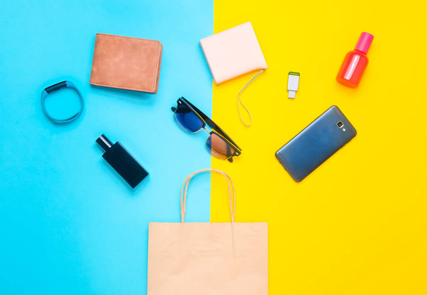Paper bags and many purchases of gadgets and accessories on a colored background: sunglasses, smartphone, smart bracelet, powel bank, usb flash drive, wallet. Consumer concept. Top view. - Photo, Image