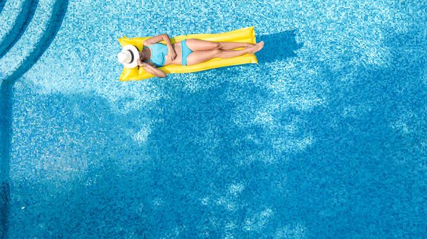 Beautiful young girl relaxing in swimming pool, swims on inflatable mattress and has fun in water on family vacation, tropical holiday resort, aerial drone view from above - Foto, imagen