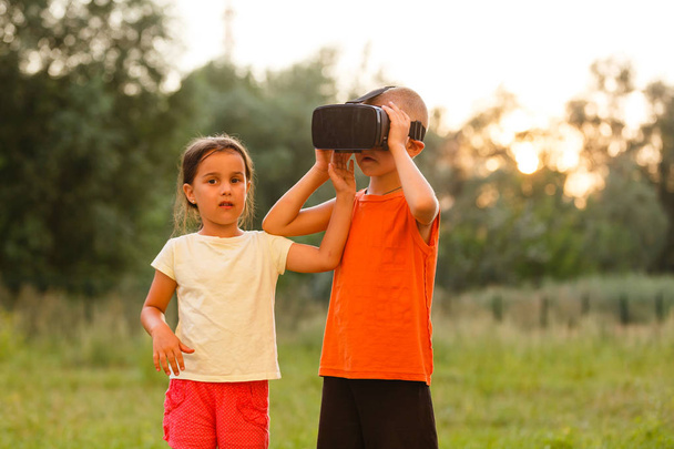 meisje met broer in virtuele werkelijkheid hoofdtelefoons samenspelen in park - Foto, afbeelding