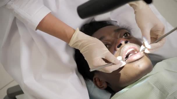 A fogorvos kezeli a beteget egy mikroszkópot. Fiatal afroamerikai férfi beteg szék, fogászati klinikán. Orvostudomány, egészség, Sztomatológia koncepció. - Felvétel, videó