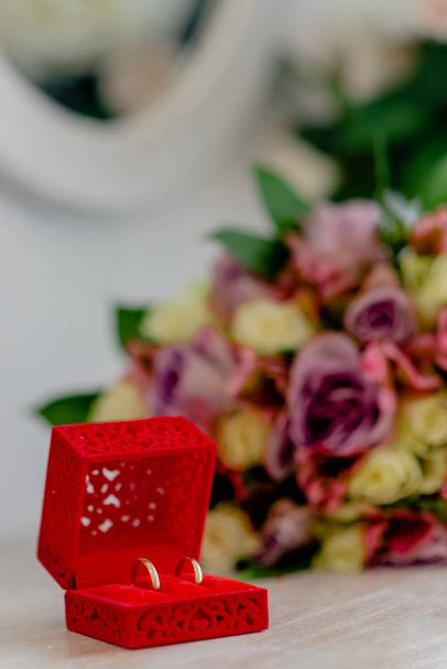 Two golden wedding rings on a wooden table in a red wedding box. With some flowers in the background.  - Foto, Imagem