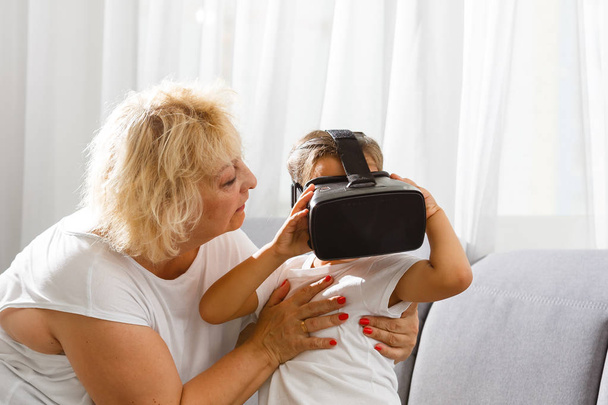 Senior woman using virtual reality glasses with granddaughter at home - Zdjęcie, obraz