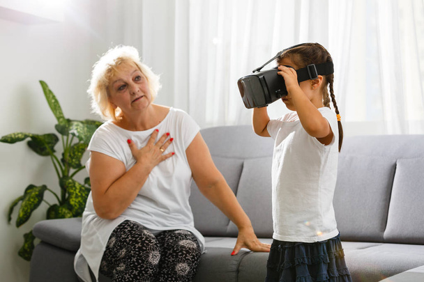 Senior woman using virtual reality glasses with granddaughter at home - Foto, Imagem