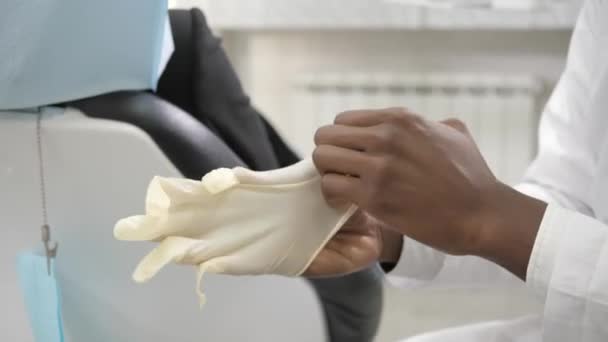 Puts on a medical medical glove and takes dental tools. Young African American male doctor dentist. Medicine, health, stomatology concept. dentist conducts inspection and concludes - Filmagem, Vídeo