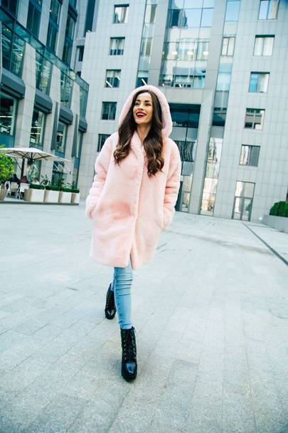 Young woman in pink fur coat walking by street - Foto, Imagem