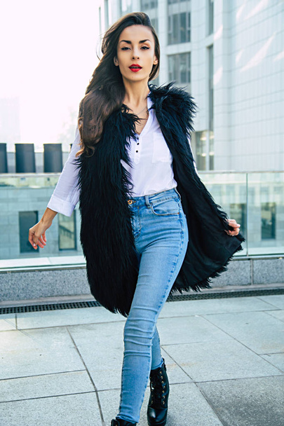Young woman in black fur vest posing on urban background - Fotó, kép