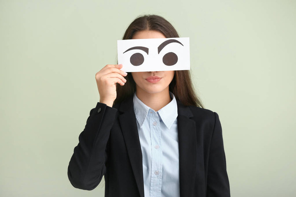 Emotionele jonge vrouw gezicht achter vel papier met getekende ogen op lichte achtergrond verbergen - Foto, afbeelding