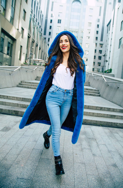 Young woman in blue fur coat walking by street - Photo, Image