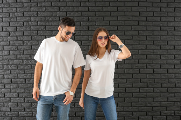 Молодий чоловік і жінка в стильних футболках проти темної цегляної стіни
 - Фото, зображення