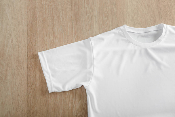 White t-shirt on wooden background, top view - Φωτογραφία, εικόνα