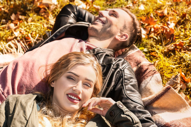 Loving young couple lying on plaid in autumn park - Fotó, kép