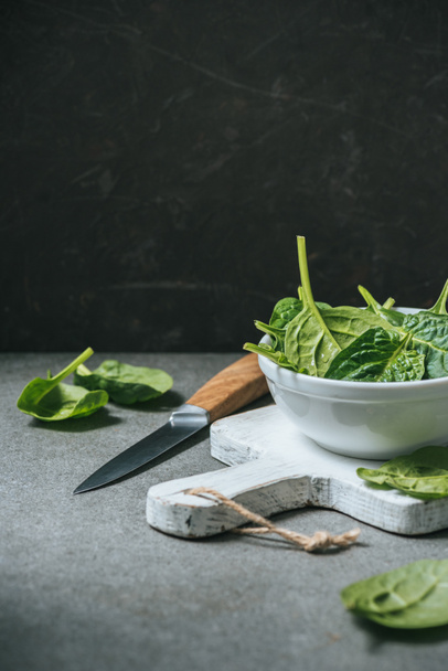 Organic fresh spinach leaves in white bowl on cutting board near metal knife - Photo, Image