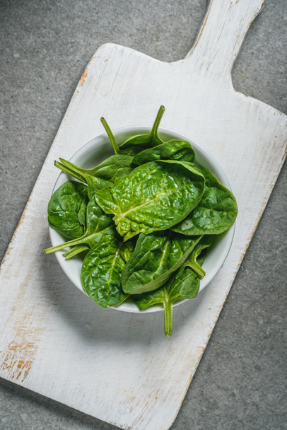 Top veiw of fresh picked spinach leaves in bowl on white cutting board  - Фото, изображение