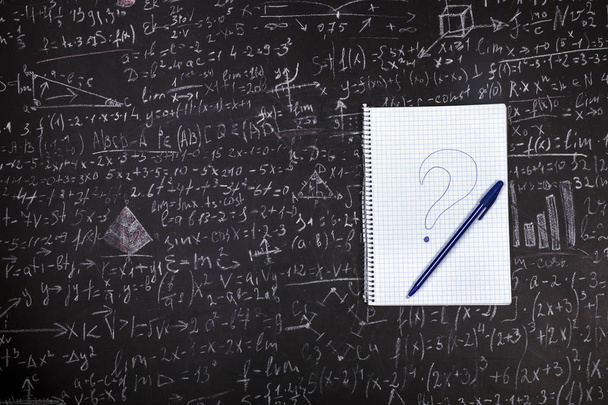 cuaderno del estudiante con un bolígrafo y un signo de interrogación en el fondo del tablero con ejemplos y fórmulas
 - Foto, imagen