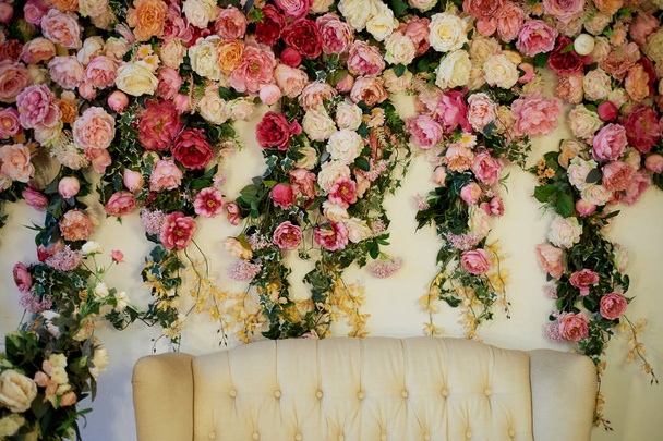 Old carved daybed with soft upholstery against a white wall decorated with pink flowers.Gorgeous garland. The interior decor is romantic, wedding photo zone. - Фото, изображение