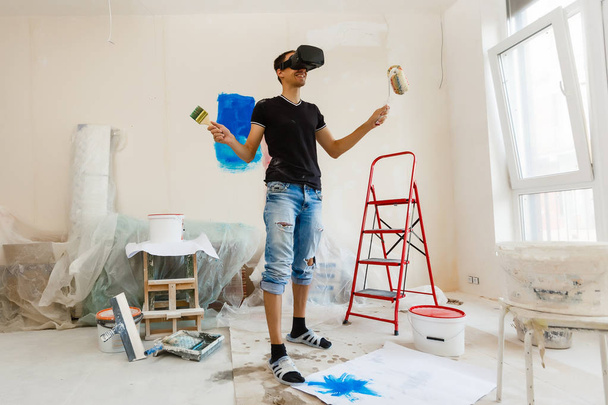 Young man in vr goggles painting wall in new apartment - Photo, Image