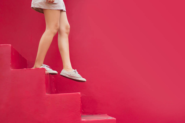 Piernas de mujer caminando por la escalera roja con espacio de copia sobre fondo rojo
. - Foto, imagen