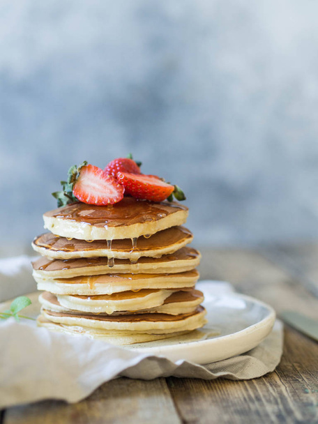 Pile of pancakes with honey and strawberries on a white plate - Fotó, kép