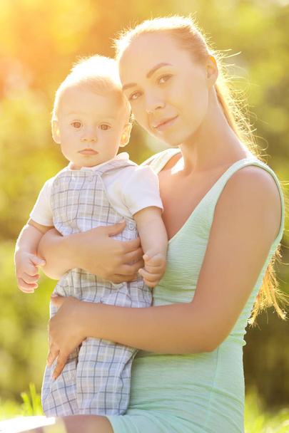 Söpö vauva kesäpuistossa äidin kanssa nurmikolla. Suloinen vauva ja äiti ulkona. Hymyilevä tunteellinen lapsi äidin kanssa kävelyllä. Lapsen hymy
 - Valokuva, kuva