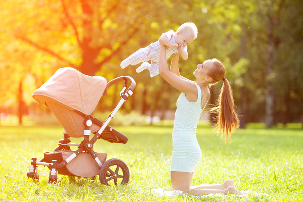 Cute little baby in summer  park with mother  on the grass. Sweet baby and mom  outdoors. Smiling emotional kid with mum on a walk. Smile of a child - Photo, Image