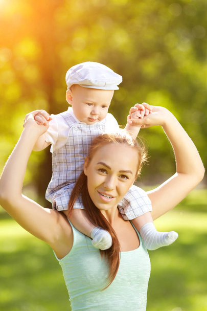 Cute little baby in the park with mother on the grass. Sweet baby and mom  outdoors. Smiling emotional kid with mum on a walk. Smile of a child - Zdjęcie, obraz
