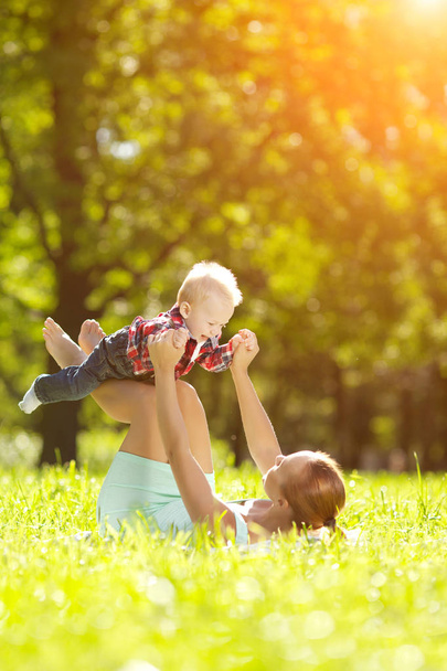 słodkie maleństwo w lato park z matki na trawie. słodkie dziecko i mama na zewnątrz. uśmiechający się emocjonalne dziecko z mamą na spacer. uśmiech dziecka - Zdjęcie, obraz