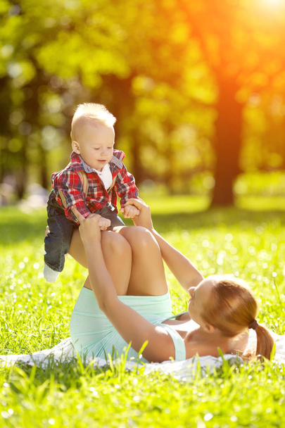 Cute little baby in summer  park with mother  on the grass. Sweet baby and mom  outdoors. Smiling emotional kid with mum on a walk. Smile of a child - Фото, изображение