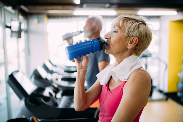 Mature woman drinking bottle of water on threadmill in gym - Фото, зображення